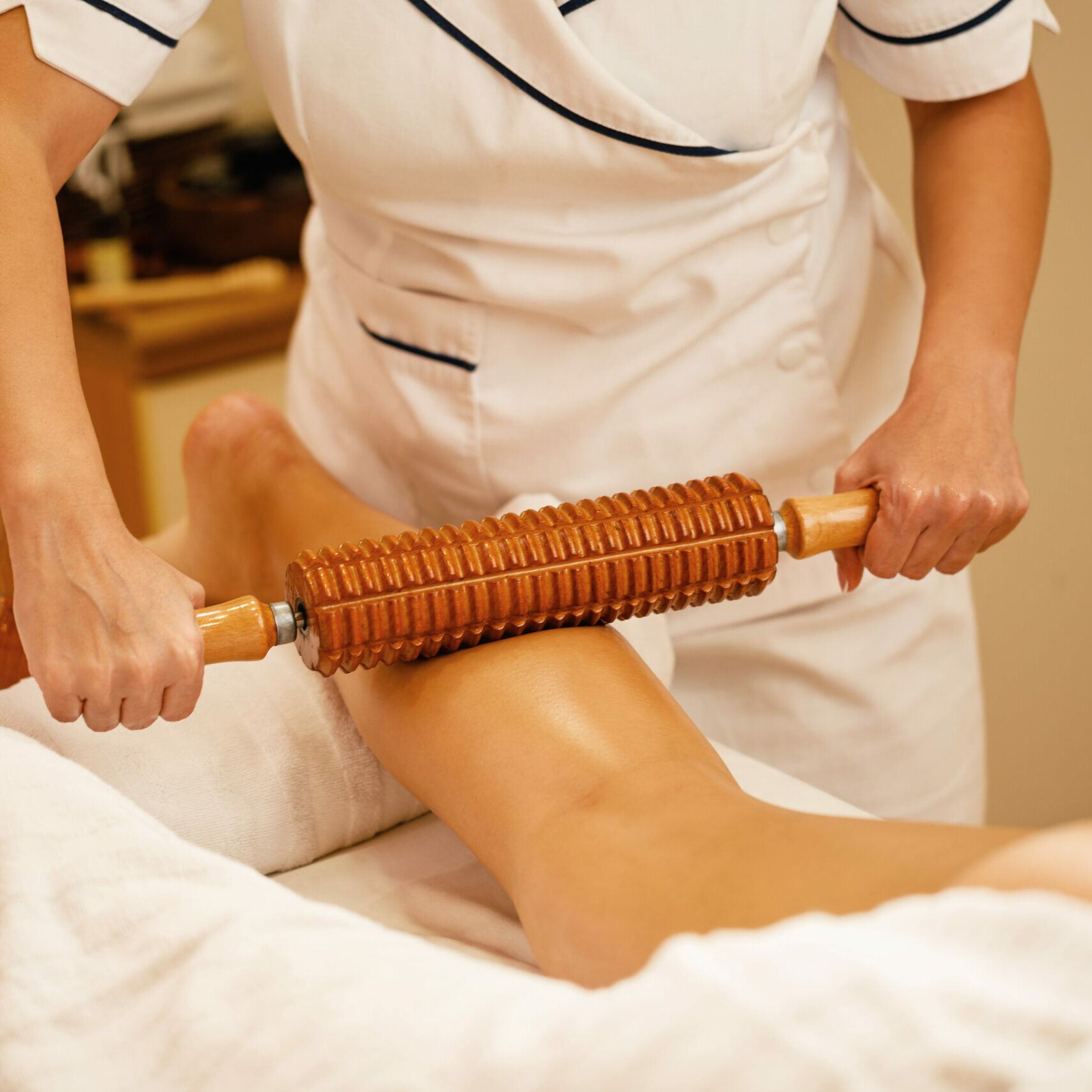 Unrecognizable therapist performing maderotherapy on woman's legs during massage treatment at the spa.